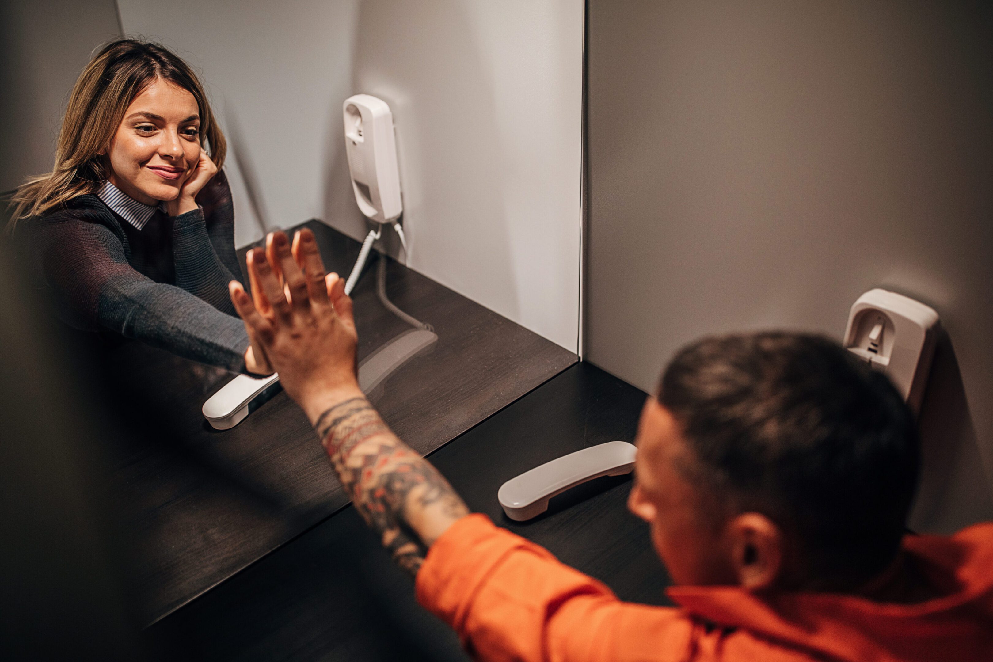 Man and woman, male prisoner talking over the phone with his wife in prison visit room.